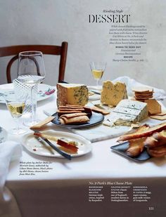 a table topped with cheese and crackers next to glasses of wine on top of a white table cloth