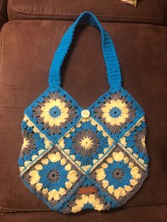 a crocheted blue and yellow purse sitting on top of a brown couch next to a remote control