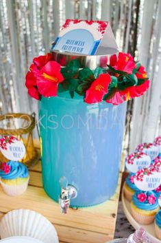 cupcakes and flowers in a blue container on a table with other desserts