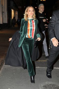 a woman is walking down the street wearing green velvet pants and a colorful top with stripes on it