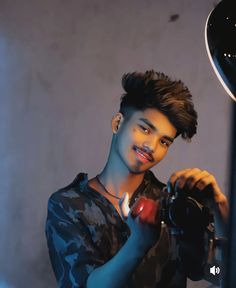 a young man holding a camera in front of a light and a microphone on a tripod