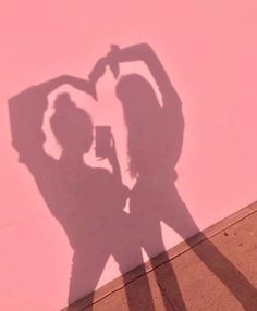 the shadow of two people standing in front of a pink wall with a coffee cup