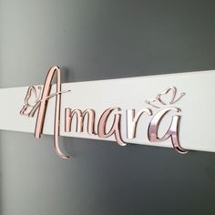 a name sign hanging on the side of a white wall with pink lettering that says amara