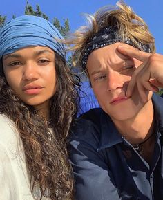 two people with bandanas on their heads posing for the camera, one is holding his head