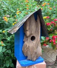 a bird house made out of wood and blue paint on top of some bricks in front of flowers