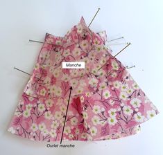 the sewing needle has been placed on top of the pink flowered dress with green and white flowers