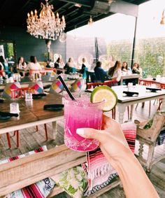 a person holding up a pink drink in front of a table with people sitting at it