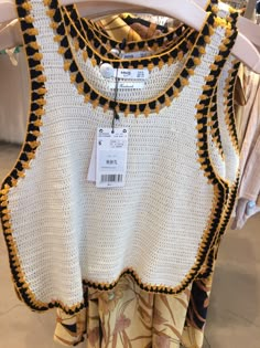 a white top with black and yellow trims hanging on a rack in a store