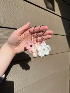 a hand holding three small crocheted flower keychains in front of a house