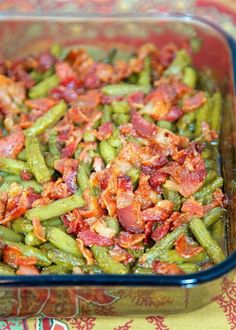 a glass dish filled with green beans and bacon on top of a colorful table cloth