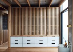 an empty room with white drawers and wooden paneling on the wall, next to a large window