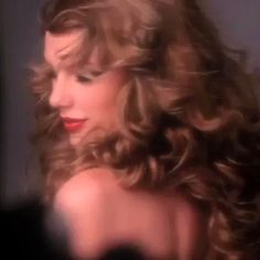 a woman with long, curly hair and red lipstick is looking down at her left shoulder