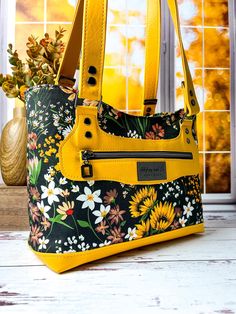 a yellow purse sitting on top of a wooden table next to a vase filled with flowers