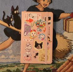 a pink notebook with stickers on it sitting on a rug next to a cat