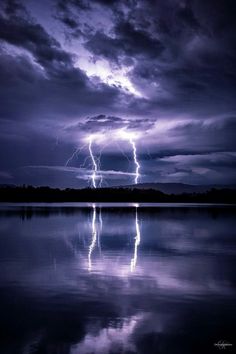 a lightning bolt is seen over the water in this dark night sky with clouds and reflections