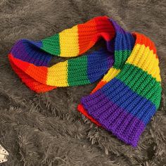 a multicolored knitted scarf laying on top of a gray blanket next to a pair of scissors