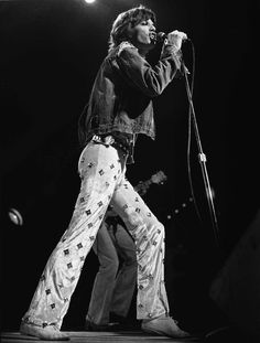 the rolling stones performing on stage in their white pants and denim jacket, holding a microphone