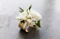 a bouquet of white flowers sitting on top of a metal table next to a gold ring