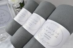 three folded gray towels with white writing on them next to a framed photo and flowers