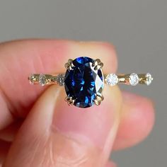 a person holding a ring with a blue stone in it's center and two white diamonds around the band