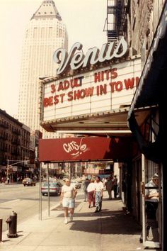 people walking on the sidewalk in front of a theater sign that reads venus, about hits best show in town