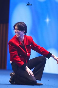 a woman sitting on the ground with her legs crossed and wearing black pants, a red jacket and white shirt