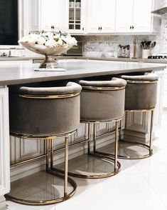 three stools in front of a kitchen island with flowers on the counter and white cabinets