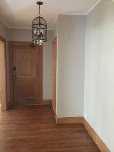 an empty hallway with wood flooring and a chandelier hanging from the ceiling