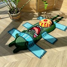 a stuffed alligator is laying on the floor next to a potted plant and rug