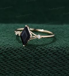 a gold ring with black onyxite and diamond accenting the band, sitting on top of a green cloth