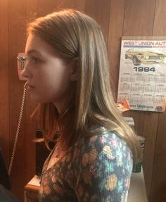 a woman with long hair and glasses is talking on the phone while standing in front of a wood paneled wall