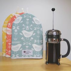 two oven mitts and a coffee pot cover on a table