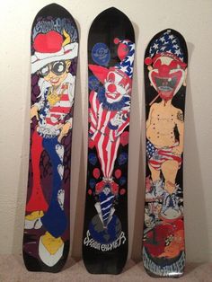 three snowboards are lined up against the wall, one with clowns on them