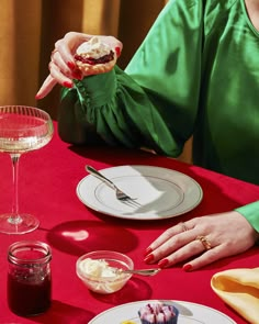 a woman sitting at a red table with food and wine in front of her,