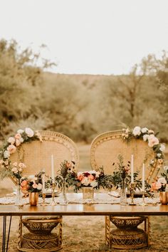 an outdoor table set up with chairs and flowers on the table, surrounded by greenery