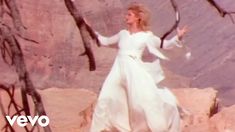 a woman in a white dress standing on rocks with her arms outstretched and hands out