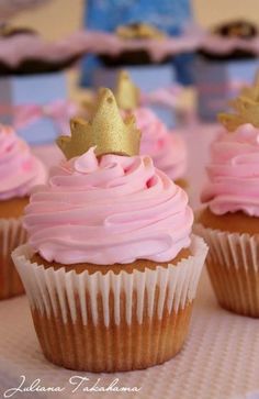 cupcakes with pink frosting and gold crowns on top are sitting on a table