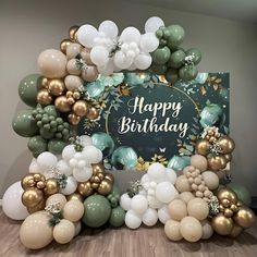 a happy birthday sign surrounded by balloons and greenery on a wooden floor in front of a wall