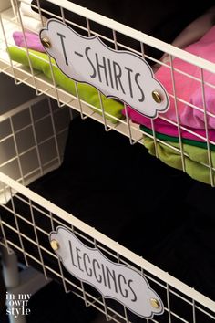 two white baskets with t - shirts hanging on the sides and labels that read t - shirts, leggings