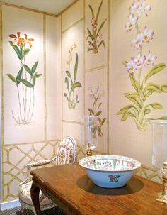 a bowl sitting on top of a wooden table next to a wall with flowers painted on it