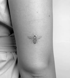 a black and white photo of a bee tattoo on the thigh, with its wings spread out