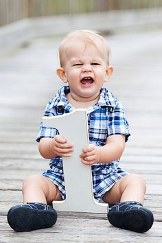 a baby boy sitting on the ground holding a white sign with his mouth open and laughing