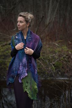 a woman standing in front of a pond wearing a purple and green shawl with leaves on it