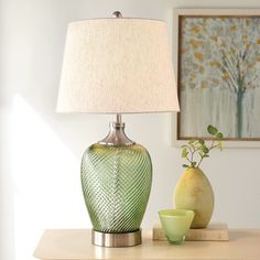 a green vase sitting on top of a table next to a lamp