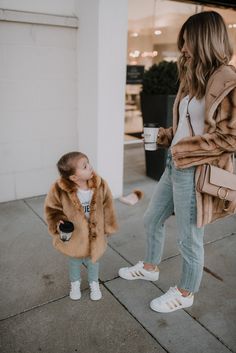 a woman and her daughter are walking down the sidewalk with coffee in their hands,