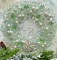 a green wreath with white pearls and pine cones