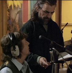 a man with long hair and headphones standing next to a woman in front of a microphone