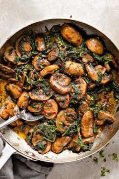 a pan filled with mushrooms and spinach on top of a white tablecloth next to a spoon