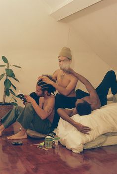 two men sitting on the floor while one man is combing another mans'hair