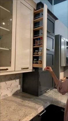 a woman standing in front of a kitchen cabinet with open shelves on the back wall